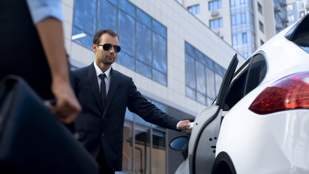 Personal driver dressed in a suit opening a car door